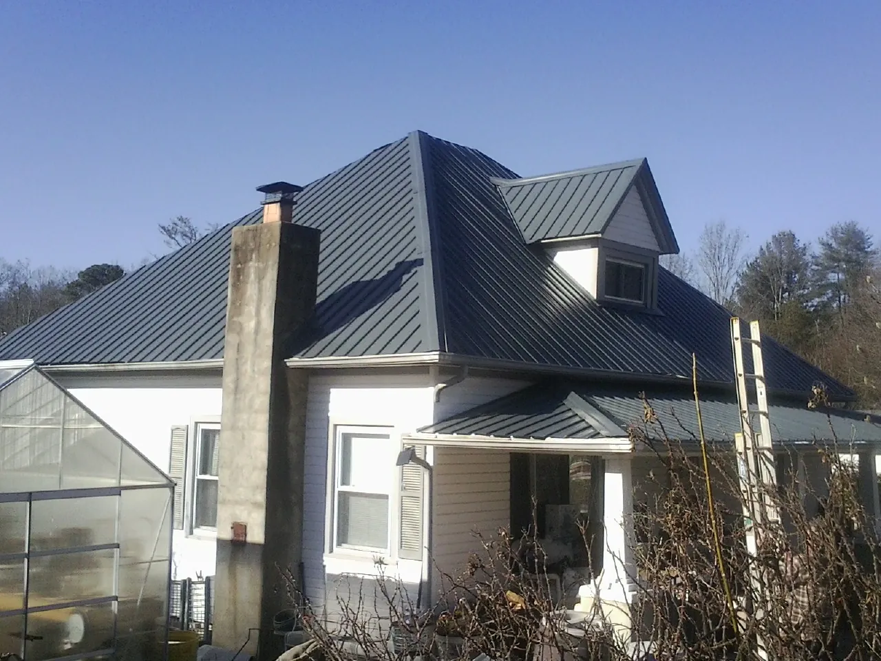 Dark blue standing seam metal roof on a white farmhouse with dormer — Slate & Tile Roof Repair by Roofing Brothers in Bellville