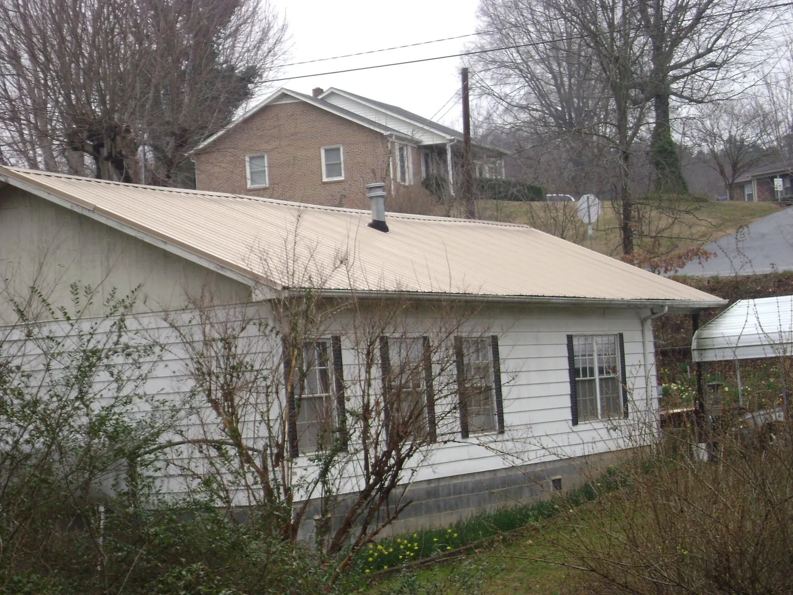 Tan metal roof on a white sided house set into a hillside — Commercial Roofing by Roofing Brothers in Bellville