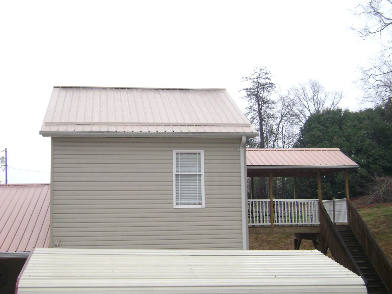 Tan metal roofs on a two story addition and attached porch, from a Roof Replacement job in Bellville